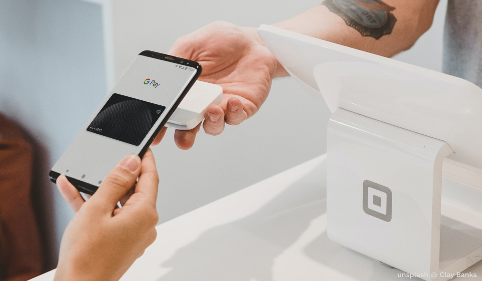 A person holding a smartphone with the Google Pay app, tapping it on a contactless payment terminal.